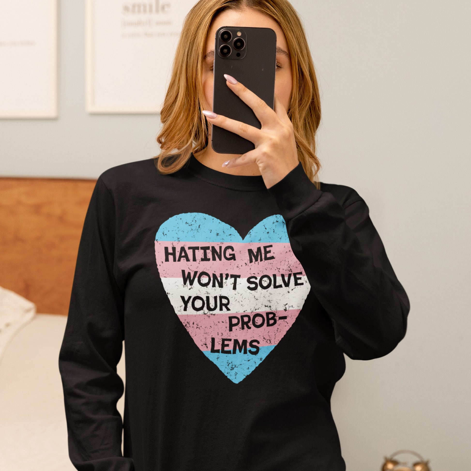Mirror selfie of a person wearing the No Trans Hate T-shirt featuring a heart in trans pride colors and “HATING ME WON’T SOLVE YOUR PROBLEMS” slogan, embodying identity and resistance.