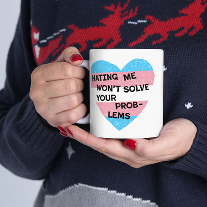 Person holds the No Trans Hate Mug, featuring a distressed-style heart in transgender pride colors with the message “HATING ME WON’T SOLVE YOUR PROB-LEMS,” embracing pride and defiance.