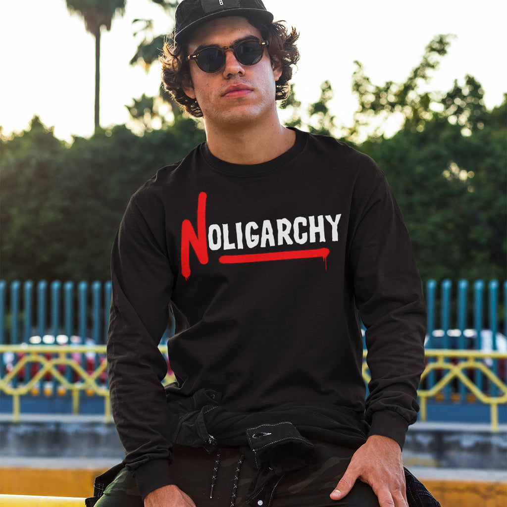 Young man outdoors in a No Oligarchy long-sleeve shirt, featuring bold white text with a red-dripping N, embodying rebellion against elitism. Perfect for those challenging the status quo.