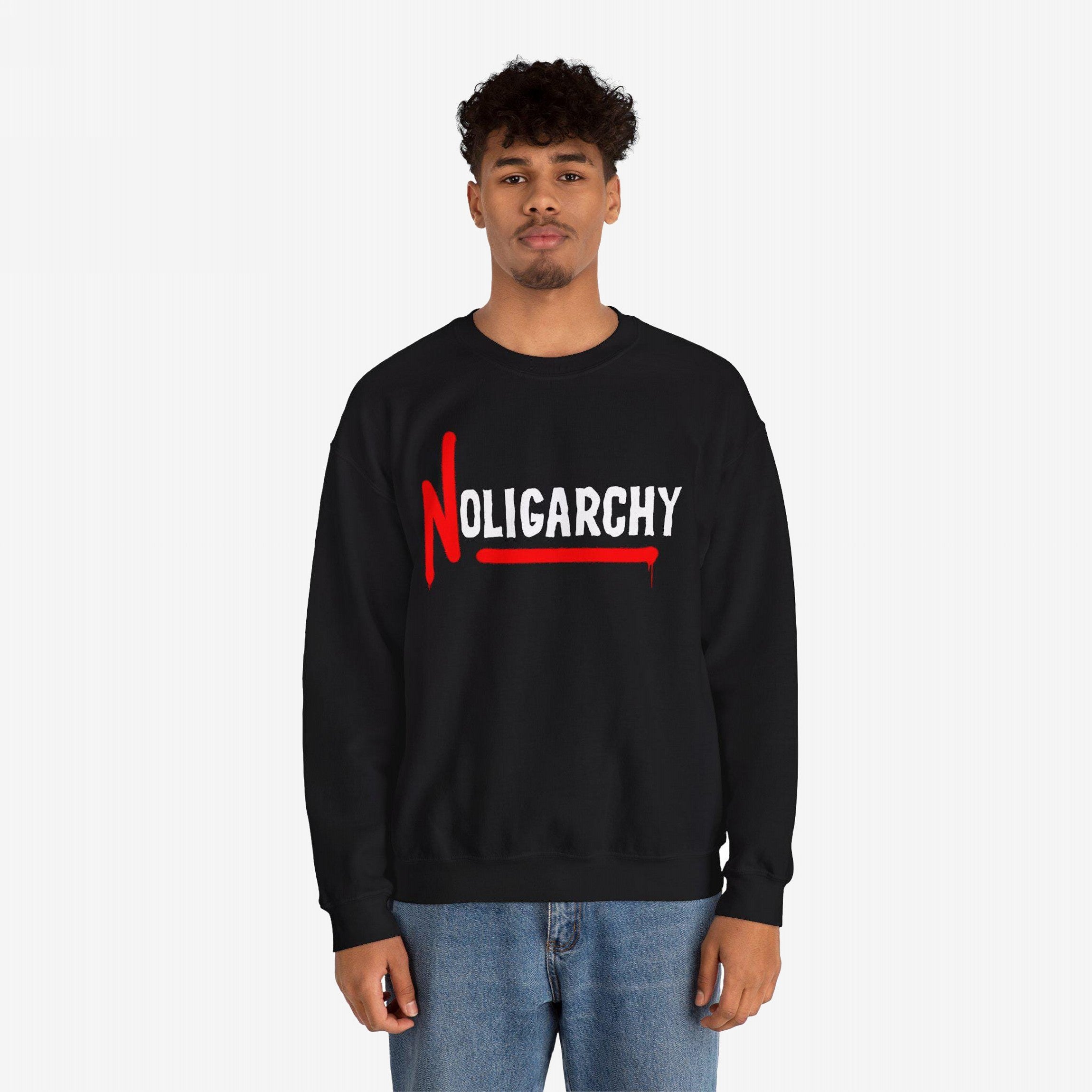 Male model wearing the No Oligarchy Shirt, featuring bold NOLIGARCHY print with a red graffiti-style N and underline, paired with blue jeans. This sweatshirt represents rebellion against elite influence.