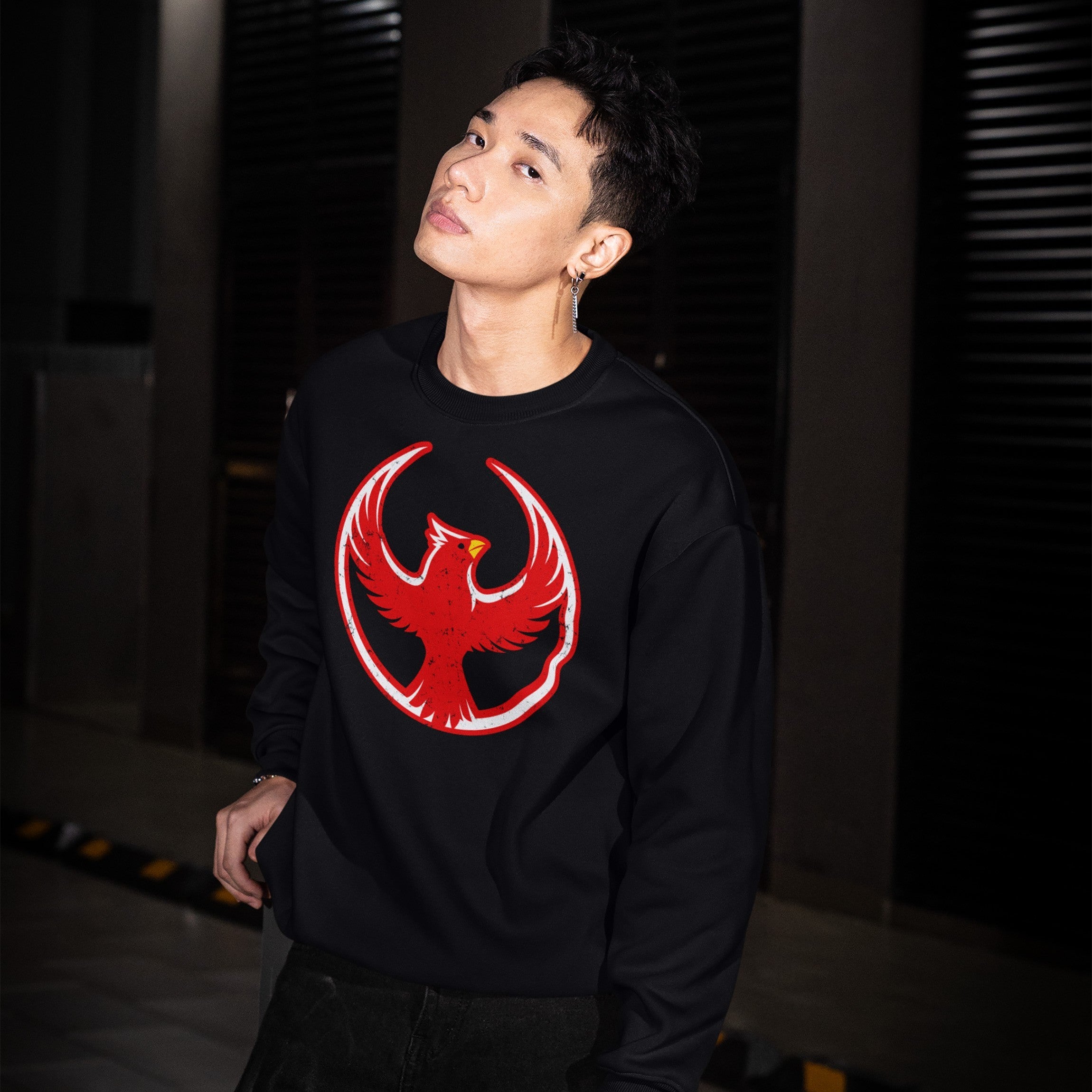 Young man in a dimly lit space wears a Northern Cardinal Rebel Alliance sweatshirt, featuring a red phoenix emblem. His gaze is confident, embodying the spirit of protest and equality.