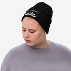 Person wearing the Not Drinking Sucks rib-knit black beanie, showcasing bold white embroidered text. Their light gray top complements the hat's confident, playful message, embodying a lively, inclusive spirit.