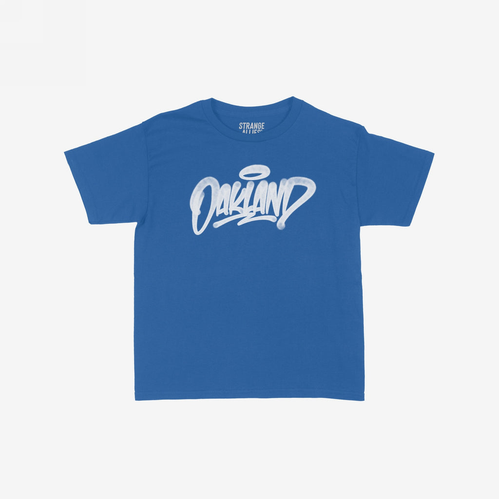 Royal-blue Oakland Handstyle Women's Baby Tee with white graffiti-style Oakland and halo accent, laid flat. Bold streetwear style, embodying confidence and local pride, perfect for urban fashion enthusiasts.