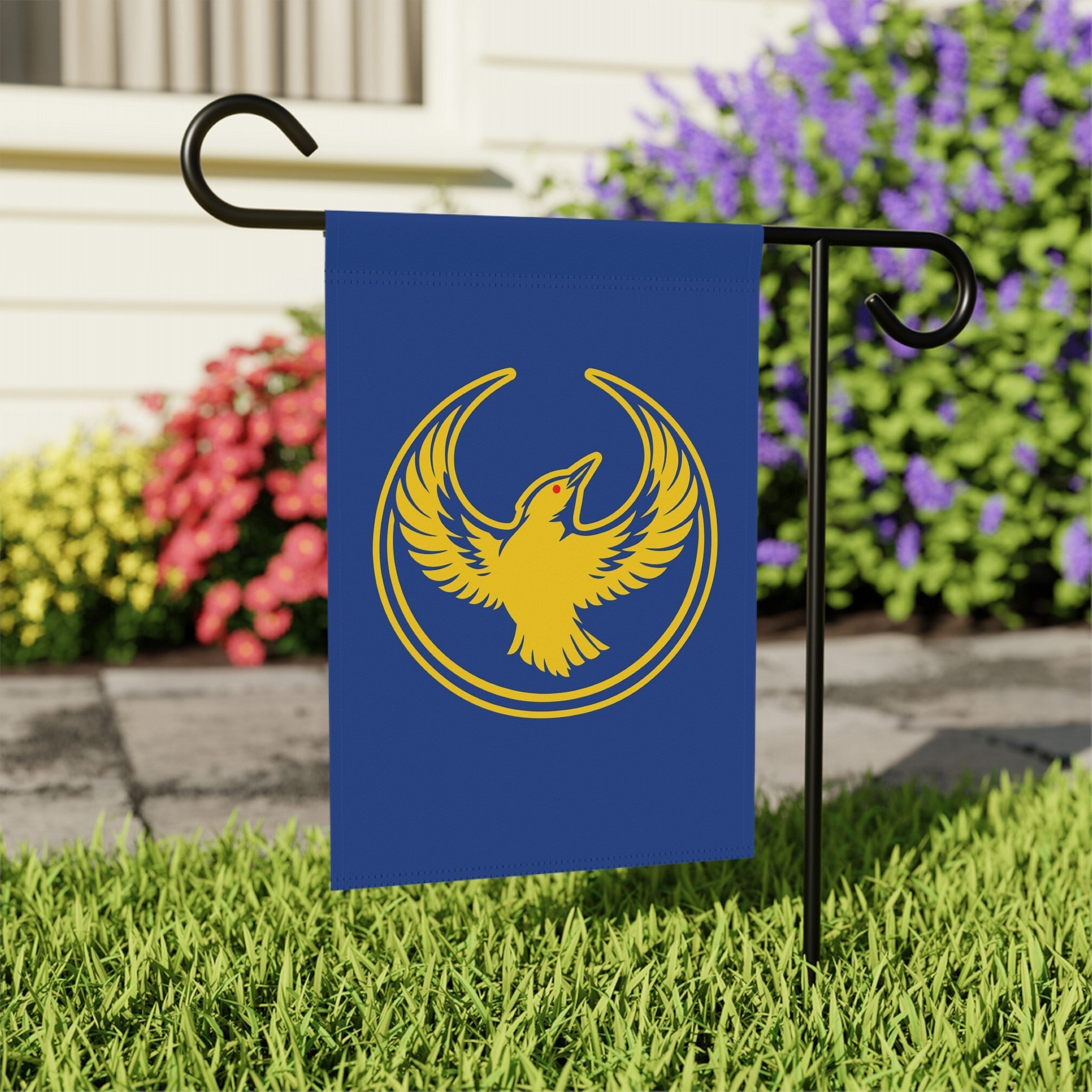 Oregon Rebel Alliance Garden Flag features a golden-yellow phoenix-like bird on a deep blue background, mounted on a black metal stand in a grassy lawn, symbolizing resistance and equality.