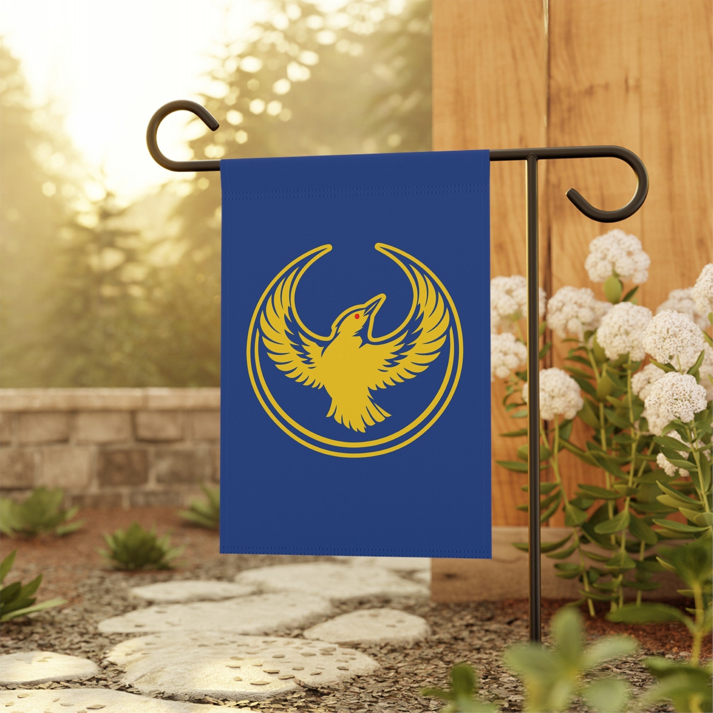 Oregon Rebel Alliance Garden Flag featuring a golden phoenix emblem on deep blue, symbolizing resistance and equality, mounted on a black stand along a stone path in a sunlit garden.