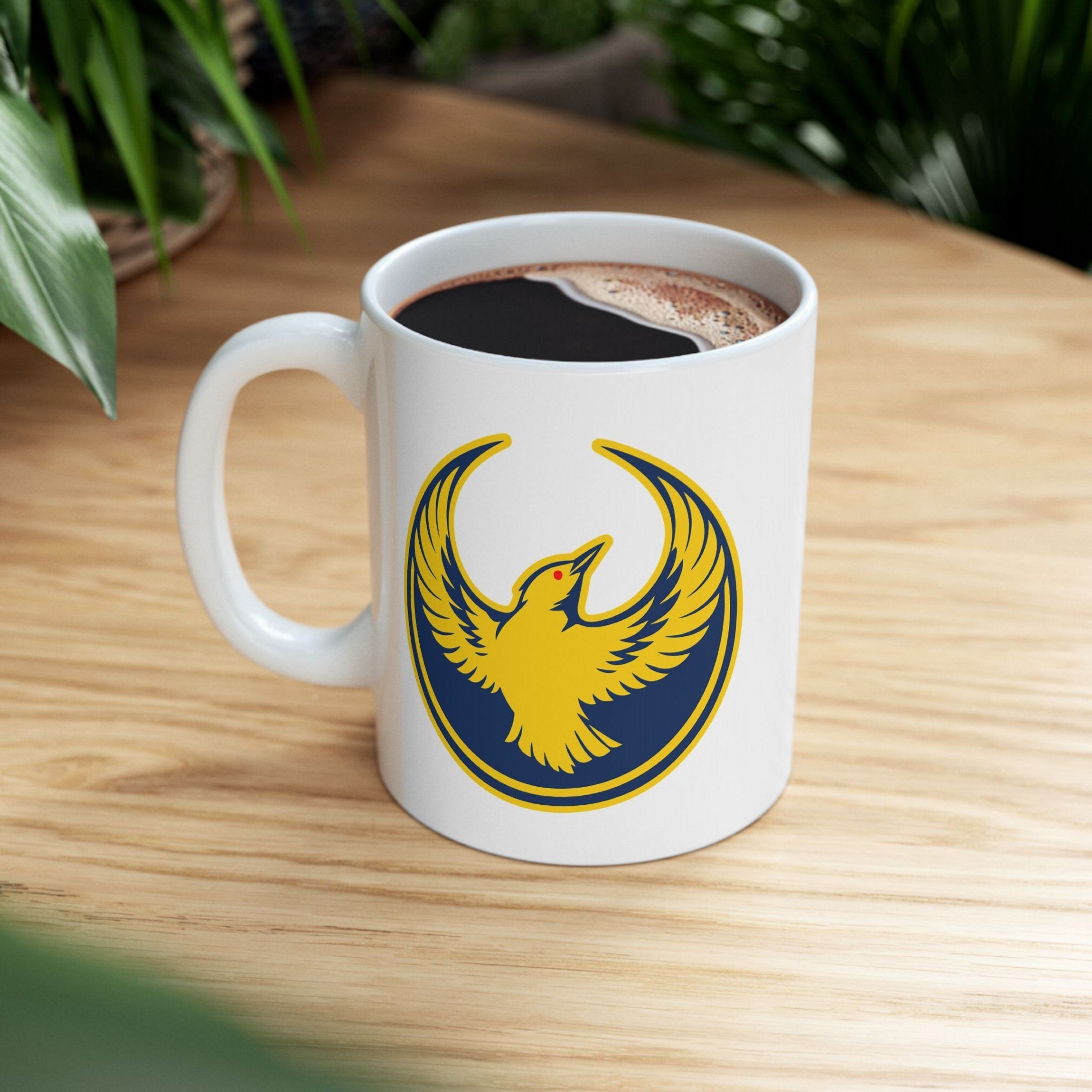 Oregon Rebel Alliance Mug featuring a golden-yellow bird emblem on a white ceramic surface, filled with black coffee, symbolizing anti-fascist and community spirit, perfect for activists and supporters alike.