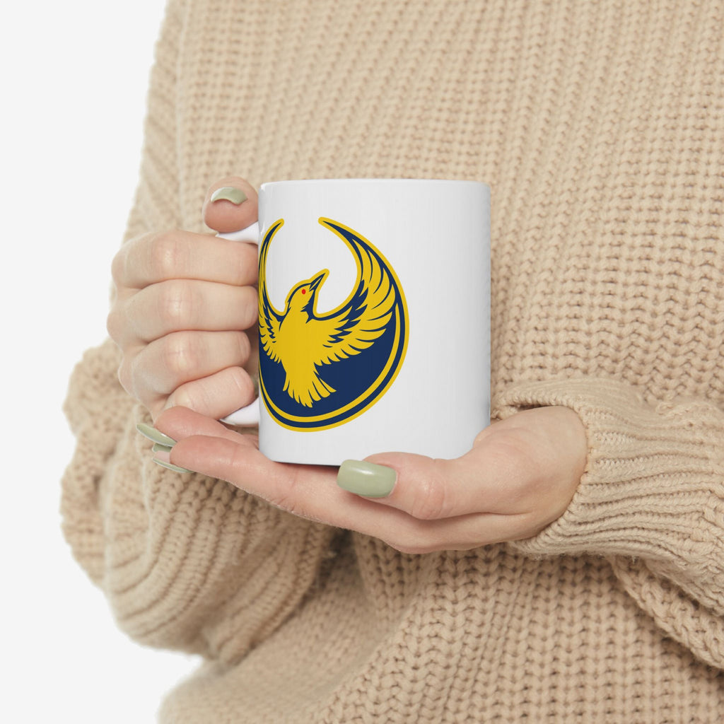 Person holding Oregon Rebel Alliance Mug, featuring a stylized bird emblem with outstretched wings on a white ceramic surface, symbolizing anti-fascist and immigrant rights support.