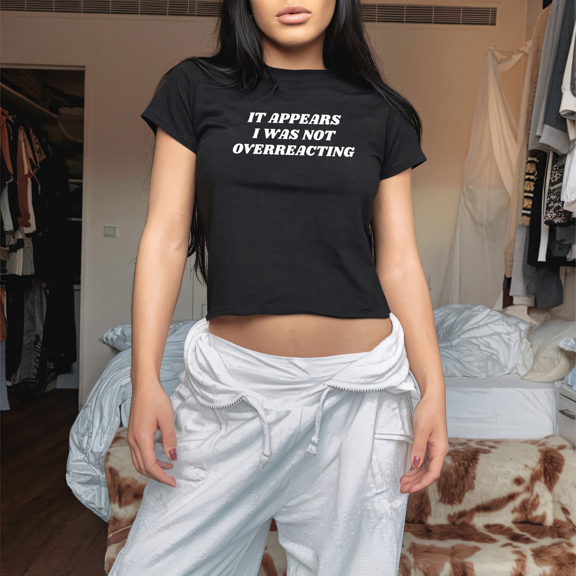 A young woman models the Overreacting Women's Baby Tee, featuring bold white lettering on a black cropped T-shirt, conveying a powerful message against oppression and silencing dissent.