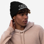 Young man in a light-beige hoodie wearing the Overreacting Hat beanie, featuring the phrase “IT APPEARS I WAS NOT OVERREACTING” on the brim, embodying anti-fascist and progressive ideals.