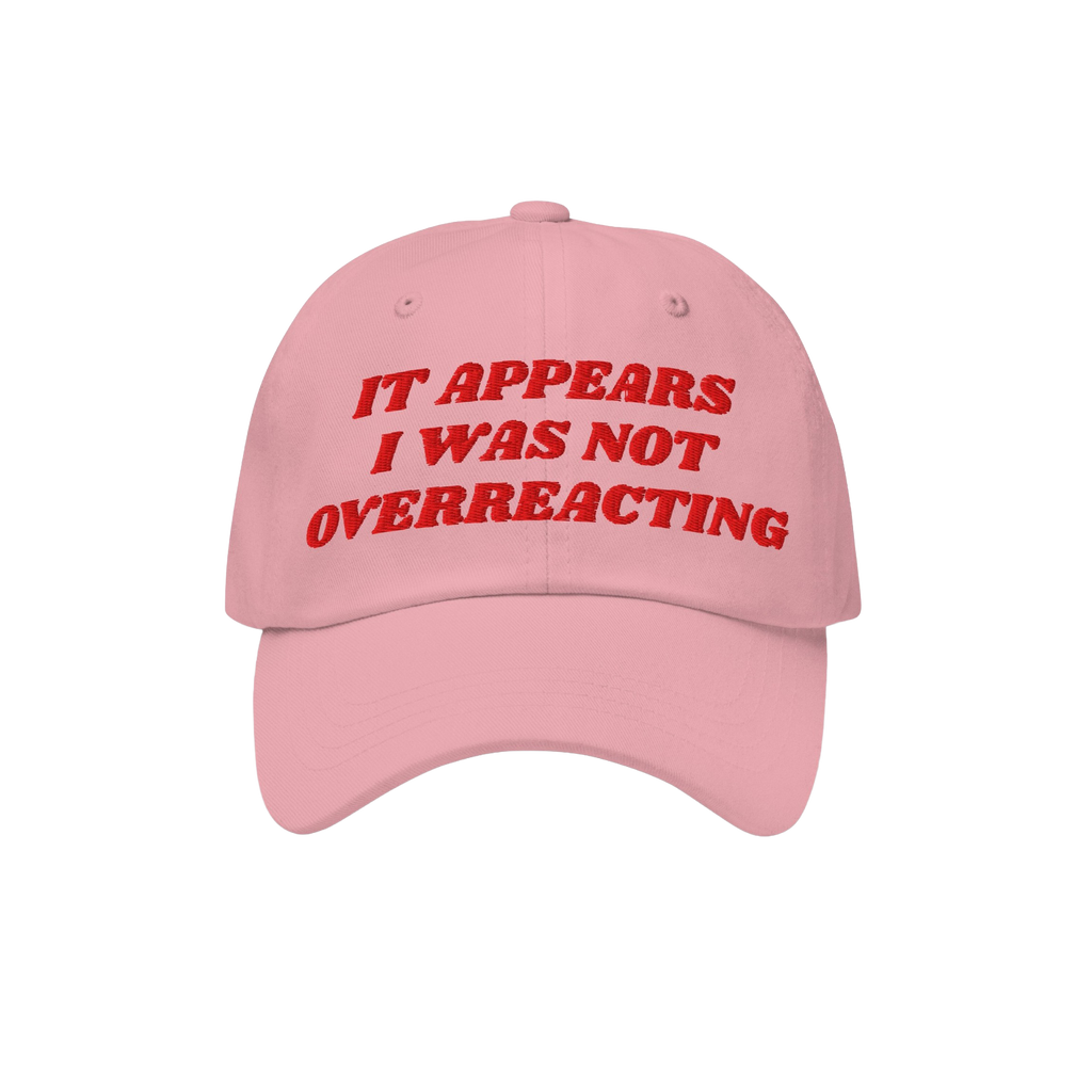 The Overreacting Hat features bold red embroidery on a light pink cap, declaring “IT APPEARS I WAS NOT OVERREACTING,” emb