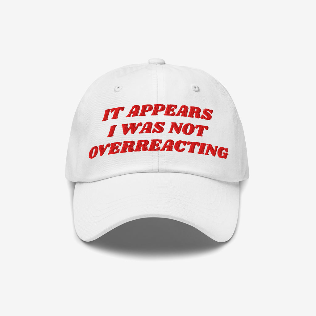 White baseball-style cap with red embroidered text: “IT APPEARS I WAS NOT OVERREACTING.” The Overreacting Hat symbolizes resistance against fascism, crafted for progressive voices.