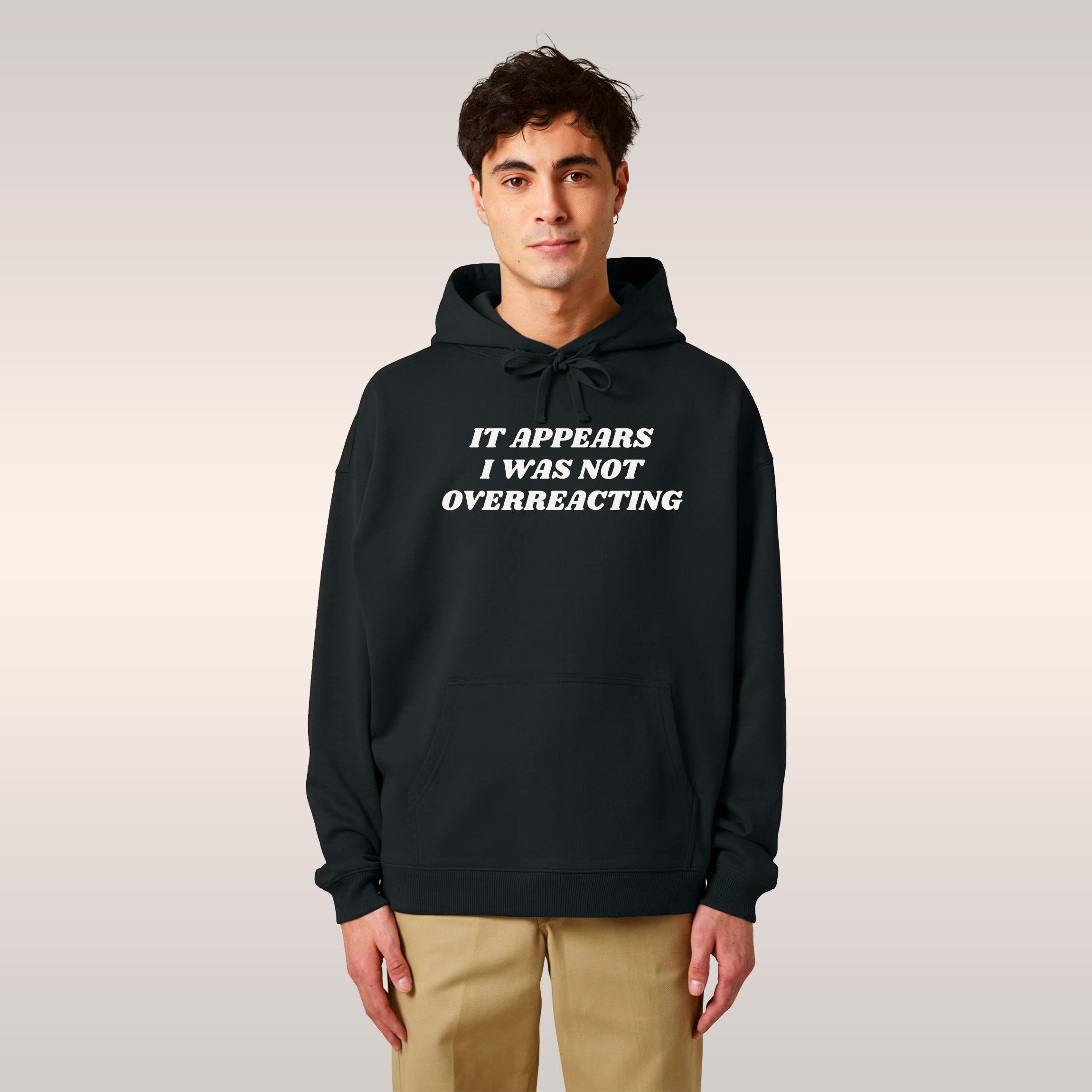 Two young Black models in urban setting, wearing hoodies with Overreacting Shirt slogan. She in pink, he in black, embodying