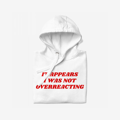 Overreacting Hoodie & Sweatshirt featuring a bold red slogan, “It appears I was not overreacting,” centered on a folded white pullover with visible hood and drawstring, embodying resistance and unapologetic critique.