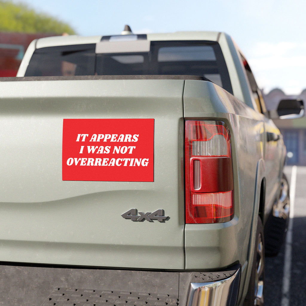 The Overreacting Sticker & Magnet is attached to a light-green 4x4 pickup truck's tailgate, featuring bold white text on a red background, advocating against political extremism and supporting progressive values.