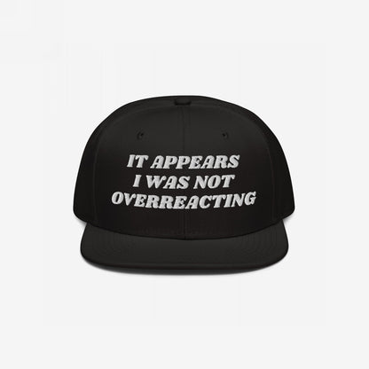 Black flat-bill snapback cap with white embroidered text: “It appears I was not overreacting.” The Overreacting Hat signifies resilience against political gaslighting, supporting progressive voices demanding justice and equality.