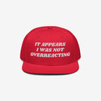 The Overreacting Hat features bold white embroidery on a red flat-brim cap, designed for progressives advocating against extremism and supporting equality.