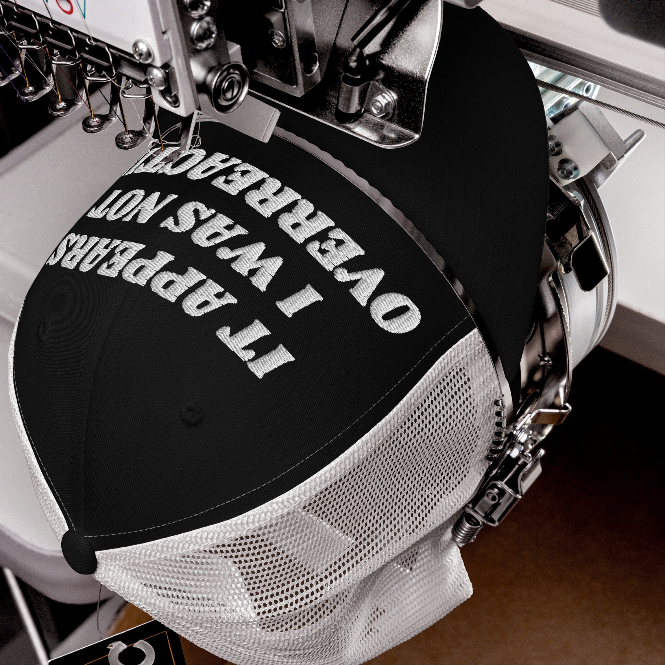 The Overreacting Hat in a trucker style is being embroidered with bold white text. This anti-fascist cap, designed for progressives, features the phrase It appears I was not overreacting.