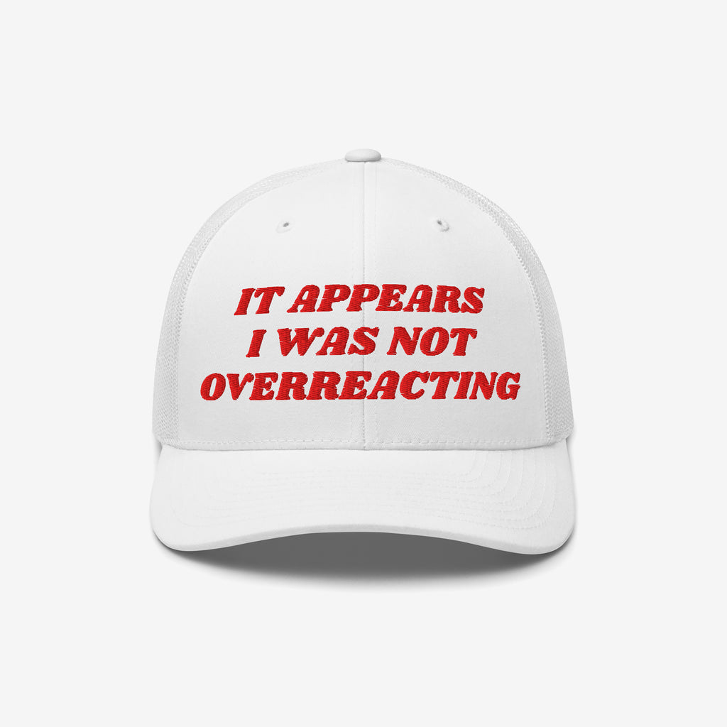 White mesh-back trucker cap, solid front with bold red embroidery: “IT APPEARS I WAS NOT OVERREACTING.” The Overreacting Hat symbolizes firm resistance against extremism and political gaslighting.