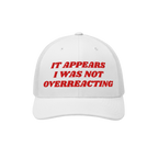 White mesh-back trucker cap, solid front with bold red embroidery: “IT APPEARS I WAS NOT OVERREACTING.” The Overreacting 