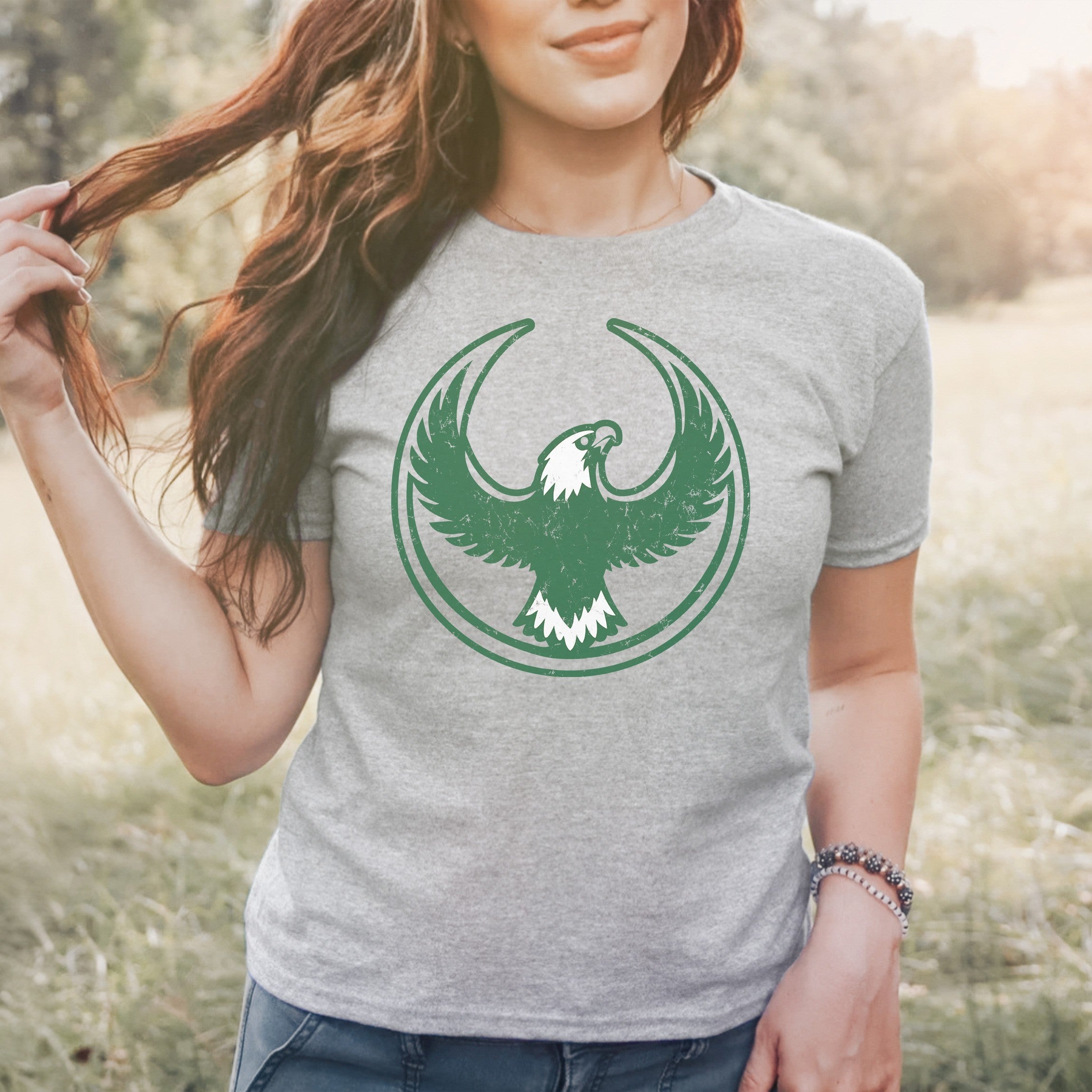Person in a grassy field wears the Philly Rebel Alliance Women's Baby Tee, featuring a green eagle emblem. The tee symbolizes protest and support for equality, matching the store's ethos of advocacy and inclusivity.