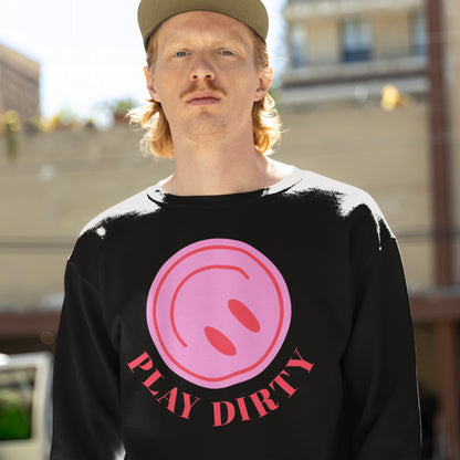 Young man in a “Play Dirty” sweatshirt with a pink graphic and bold red slogan, embodying mischief and subversion, set against an urban backdrop.