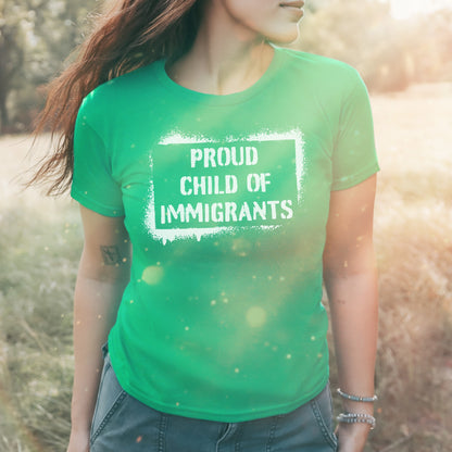 A person outdoors wearing the Proud Child Of Immigrants Women's Baby Tee, showcasing a bold message in white. The vibrant T-shirt celebrates cultural heritage and migration, embodying confidence and identity.