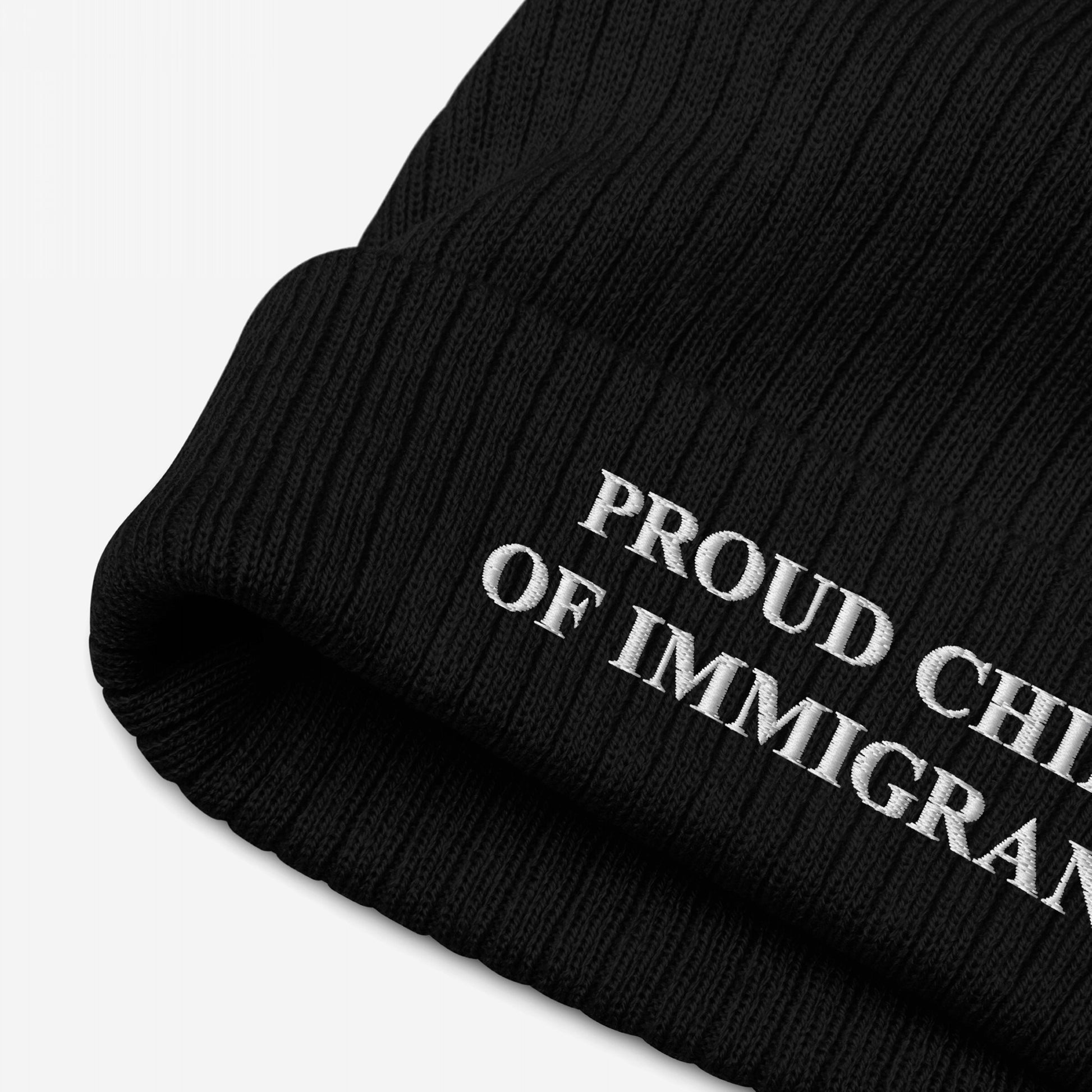 Close-up of the Proud Child of Immigrants Hat, a black ribbed knit beanie featuring white embroidered text. This hat boldly represents identity and heritage, embodying resilience and pride.