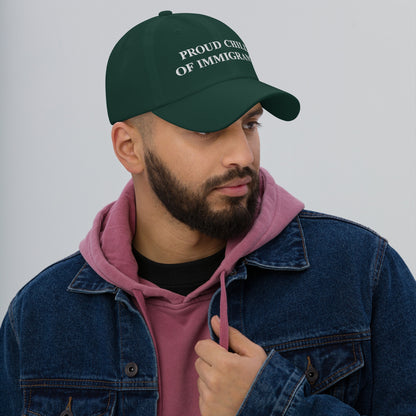 A man wears the Proud Child of Immigrants Hat, a dark green cap with impactful embroidered text, paired with a pink hoodie and denim jacket, embodying resilience and pride.