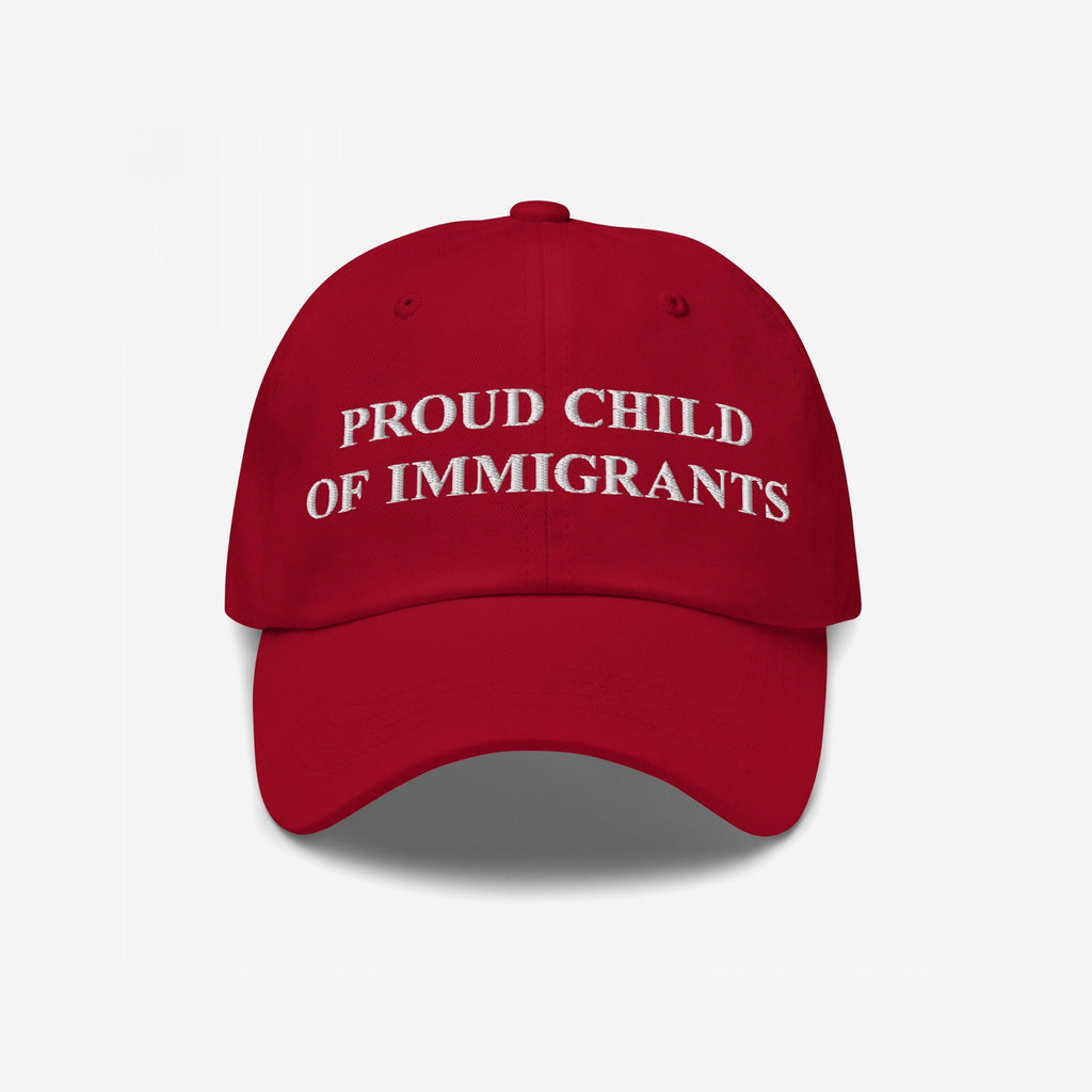 Red baseball cap with white embroidered PROUD CHILD OF IMMIGRANTS text, embodying resilience and pride; a statement piece for those honoring roots and challenging injustice through bold identity.