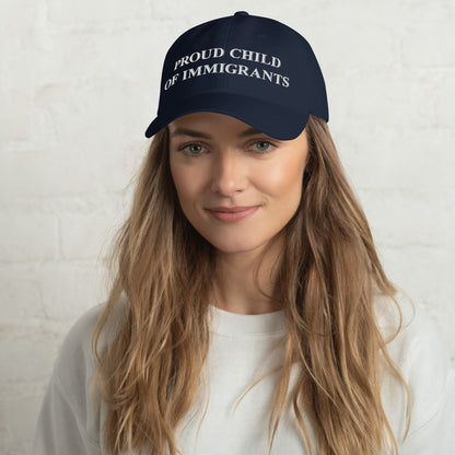 Young woman wearing the Proud Child of Immigrants Hat, featuring bold white embroidery on a navy baseball cap, embodying a statement of heritage and resilience.