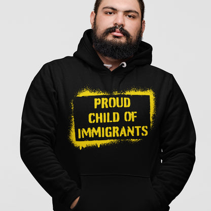 Proud Child Of Immigrants Hoodie features a spray-painted yellow frame with bold text, worn by a person with a dark beard and septum piercing, embodying heritage and identity.
