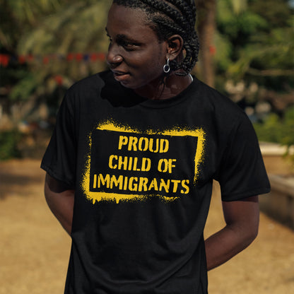 Young person outdoors wearing a Proud Child of Immigrants T-shirt, featuring bold yellow lettering, representing cultural pride and strength. The shirt embodies belonging and shared stories across generations.