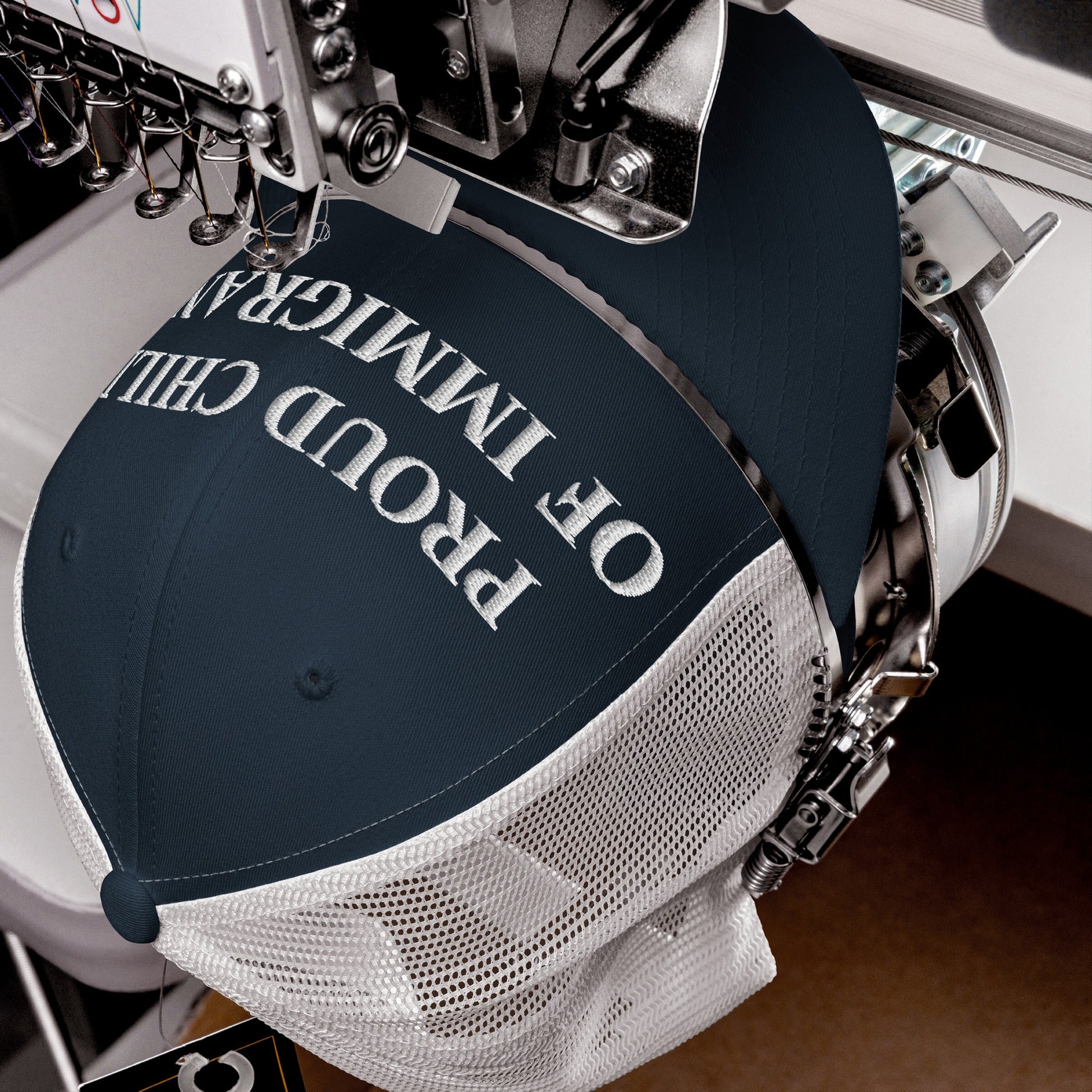 Proud Child of Immigrants Hat in embroidery setup, showcasing bold white stitching on navy, symbolizing heritage and resilience. The trucker cap combines minimalist style with a powerful identity statement.