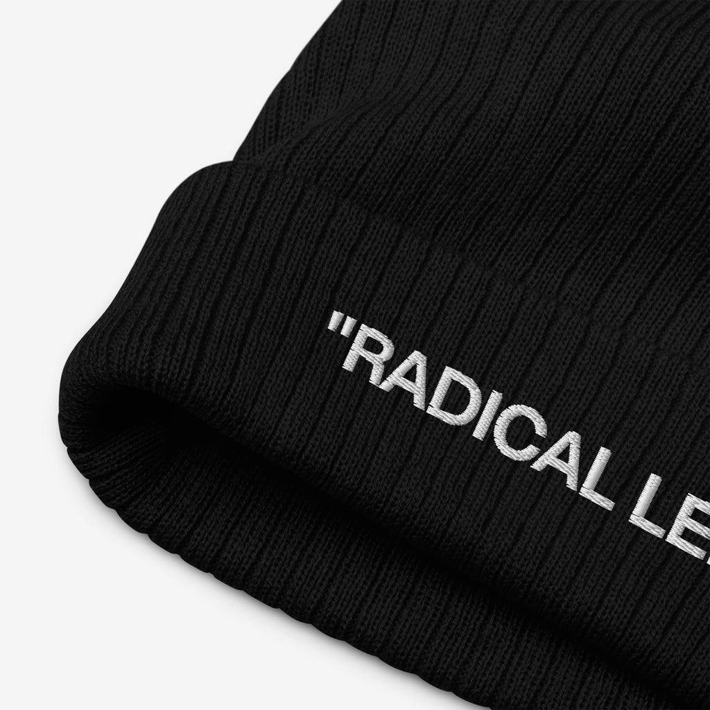 Close-up of the Radical Left Classic Hat, a black rib-knit beanie with a folded cuff, featuring white embroidered RADICAL LE. text, embodying progressive identity with irony and style.