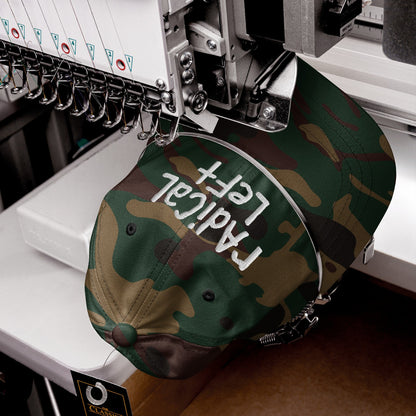 Camo-print baseball cap in embroidery machine, stitching Radical Left on front. Hang tag reads “CLASSIC.” Part of a collection promoting equality and progress.