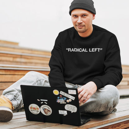 Man in light-wash jeans and boots wears Radical Left sweatshirt, embodying activism and equality while working on a sticker-covered laptop, reflecting the store's commitment to social justice and empowerment.