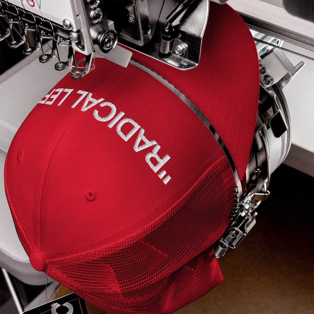 Industrial embroidery machine stitching RADICALE on a red mesh-back trucker cap, part of the Radical Left Classic Hat collection. Ideal for those embracing progressive identities with style and irony.
