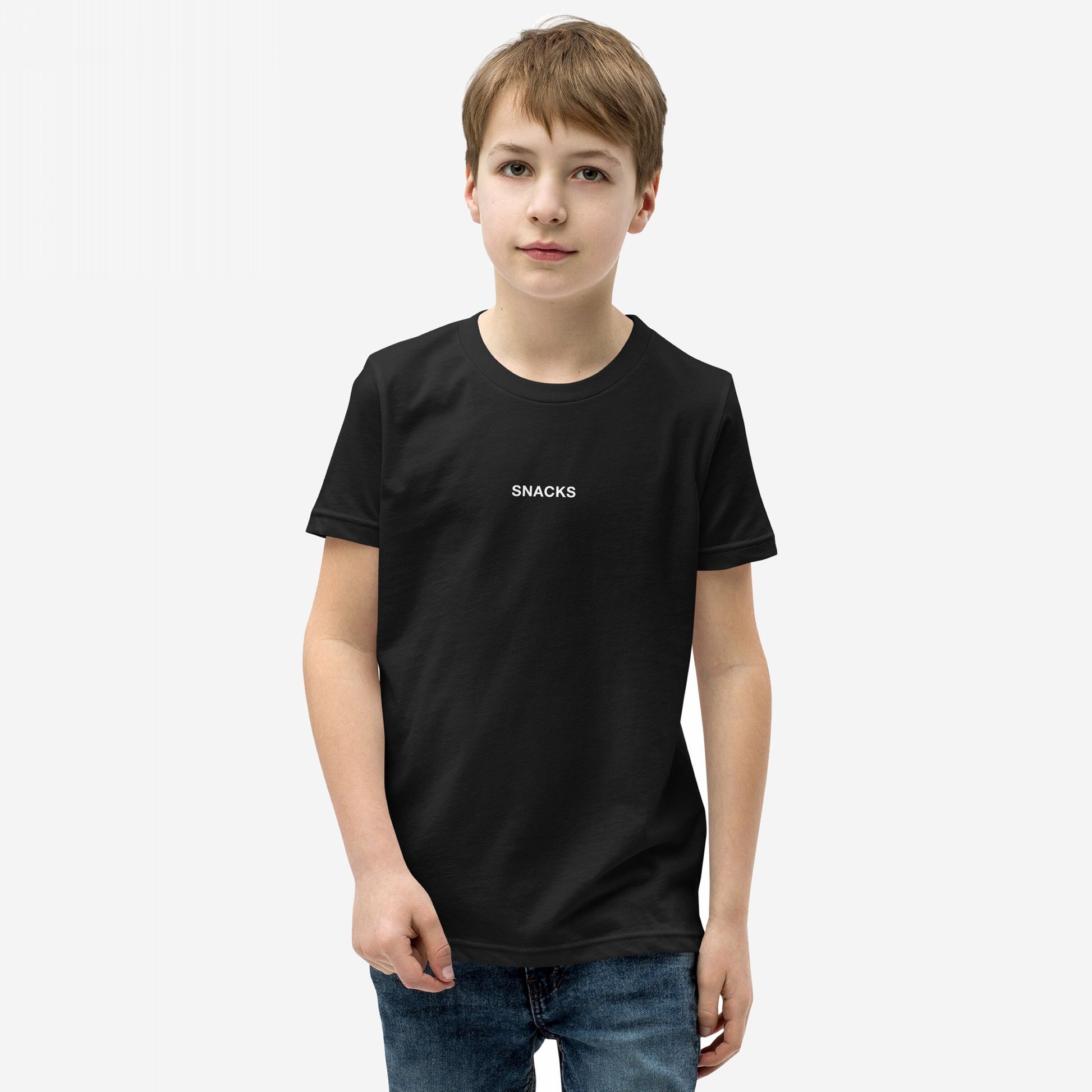 Young boy models the Snacks T-shirt, featuring subtle SNACKS text, embodying a playful, rebellious spirit. Perfect for every snack lover, it’s an enigmatic fashion statement for all ages.