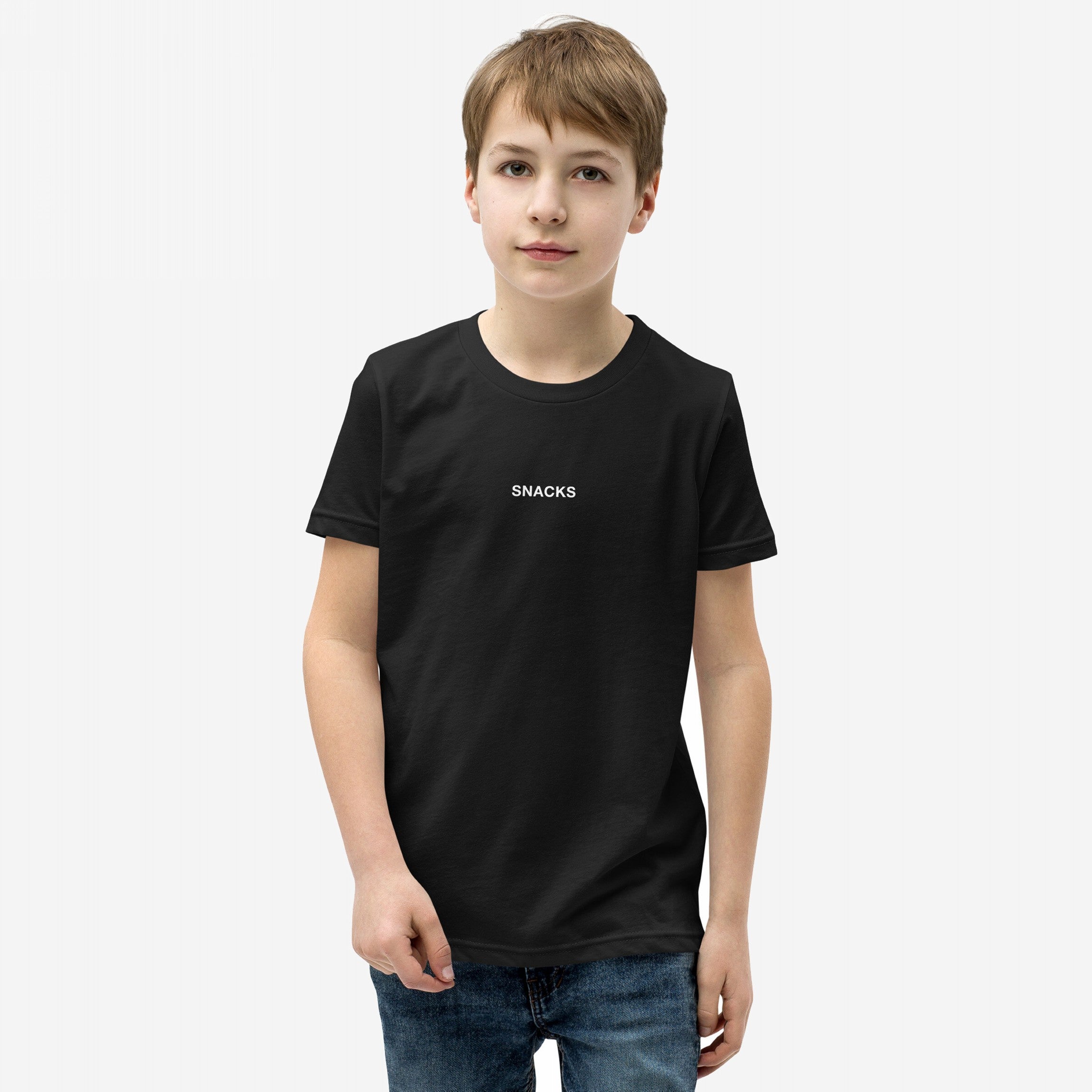 Young boy models the Snacks T-shirt, featuring subtle SNACKS text, embodying a playful, rebellious spirit. Perfect for every snack lover, it’s an enigmatic fashion statement for all ages.