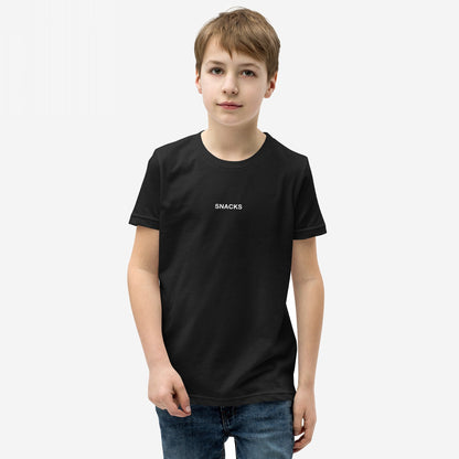 Young boy models the Snacks T-shirt, featuring subtle SNACKS text, embodying a playful, rebellious spirit. Perfect for every snack lover, it’s an enigmatic fashion statement for all ages.