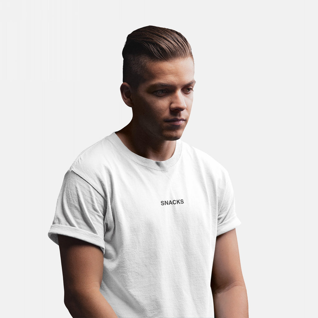 Young man wearing the Snacks T-shirt, featuring small uppercase lettering on the chest. His slicked-back hair and relaxed pose complement the tee’s understated, cryptic vibe, perfectly embodying playful yet bold fashion.