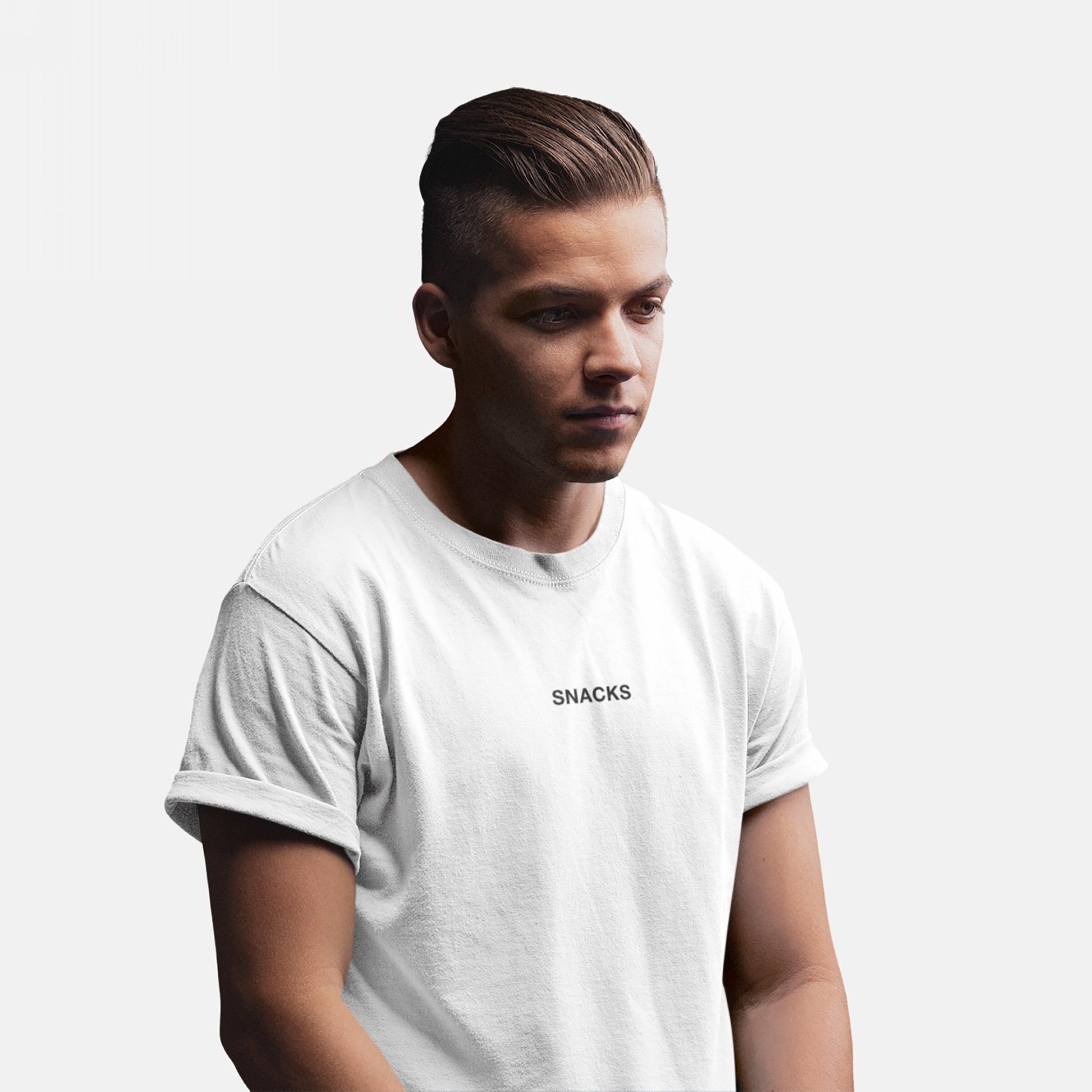 Young man wearing the Snacks T-shirt, featuring small uppercase lettering on the chest. His slicked-back hair and relaxed pose complement the tee’s understated, cryptic vibe, perfectly embodying playful yet bold fashion.