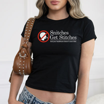 Young woman in a fitted Snitches Get Stitches Women's Baby Tee with bold text critiquing healthcare, paired with light-wash jeans and a studded leather shoulder bag, embodying edgy, socially conscious style.