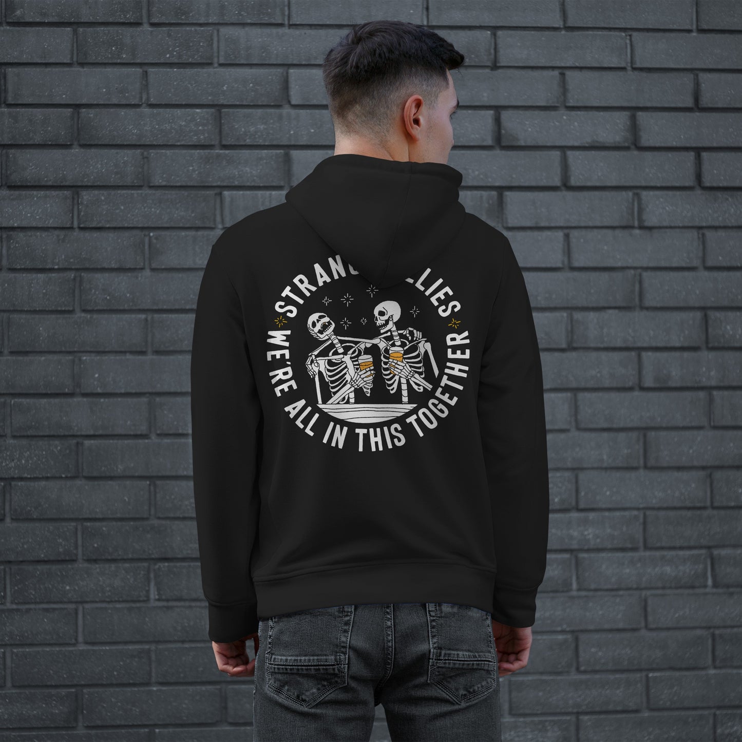A person wearing the Social Club Hoodie & Sweatshirt with a bold back print of skeletons clinking mugs, signaling camaraderie with the slogans “STRANGE BUDDIES” and “WE’RE ALL IN THIS TOGETHER.”