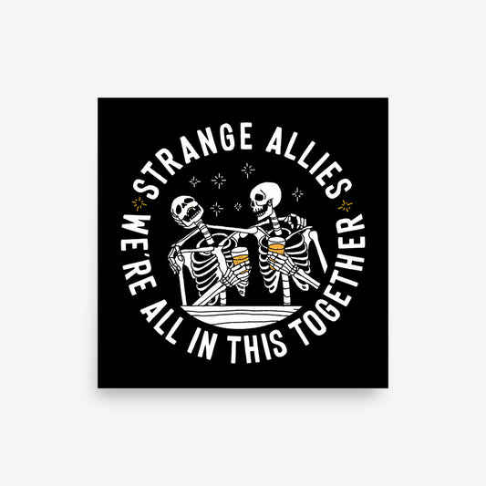 Social Club Giclée Print featuring two skeletons toasting with beer mugs, encircled by the phrase We're All in This Together, promoting inclusivity and camaraderie. Available in multiple square sizes.