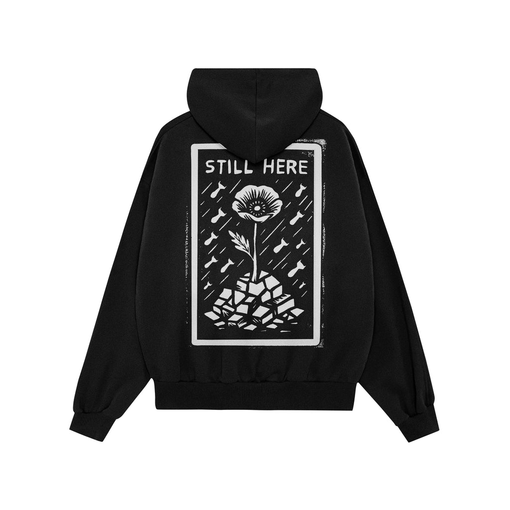 Still Here JULZ Hoodie featuring a bold graphic of a resilient flower growing through rubble amid falling shapes, symbolizing