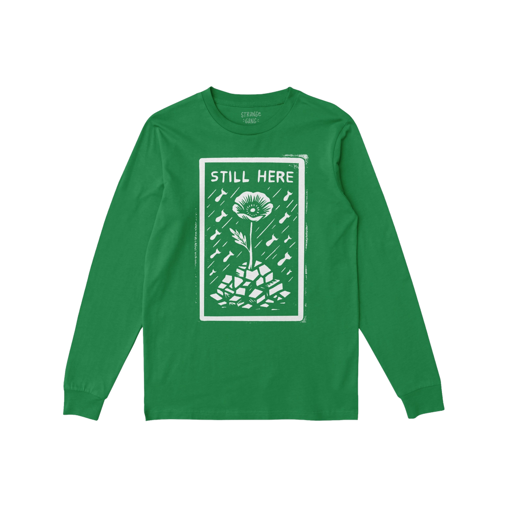 Still Here T-shirt: Green long-sleeve featuring a bold design with 'STILL HERE' text, a poppy flower emerging from rubble, su