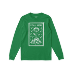 Still Here T-shirt: Green long-sleeve featuring a bold design with 'STILL HERE' text, a poppy flower emerging from rubble, su