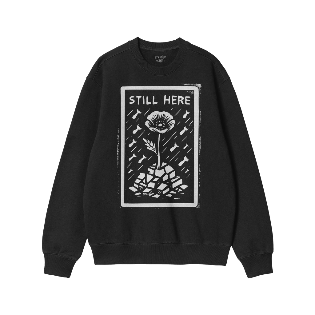 Still Here JULZ Hoodie & Sweatshirt displays a flower emerging from rubble amid falling raindrops, symbolizing resilience and