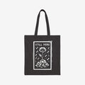 The Still Here Tote Bag displays a white hand-drawn flower rising from stones amid falling rain, symbolizing resilience against adversity. Ideal for activists, it's a powerful statement against oppression.